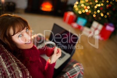 Pretty redhead holding mug of hot drink and laptop