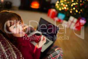 Pretty redhead holding mug of hot drink and laptop
