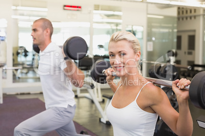 Sporty young couple lifting barbells in gym