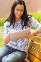 Happy brunette sitting on bench using tablet pc