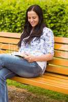 Smiling brunette sitting on bench reading