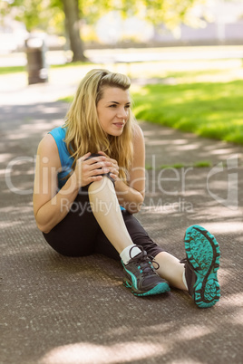 Fit blonde touching her injured knee on path