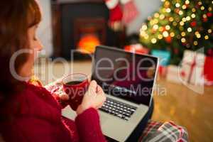 Redhead holding hot drink and using laptop