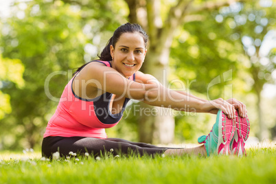 Happy brunette in sportswear stretching on the grass