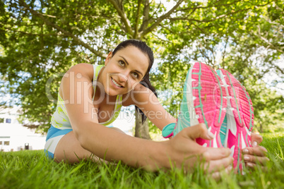 Smiling brunette in sportswear stretching on the grass