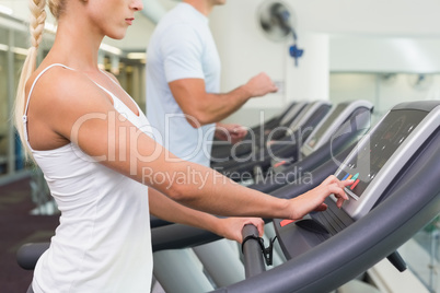 Side view mid section of couple running on treadmills at gym