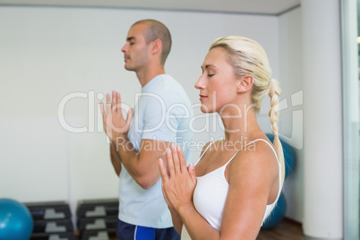 Couple with joined hands and eyes closed at fitness studio