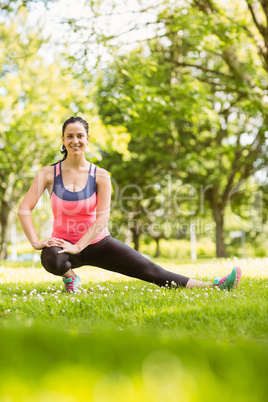 Happy fit brunette stretching on grass