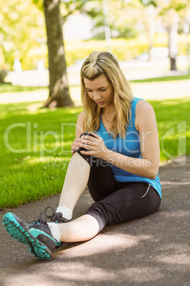 Fit blonde touching her injured knee on path