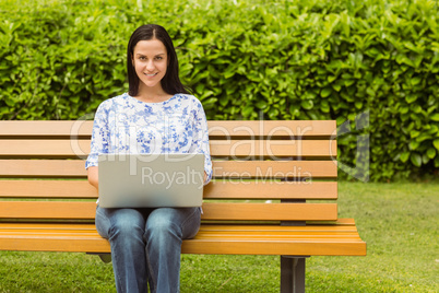 Cheerful brunette sitting on bench using laptop