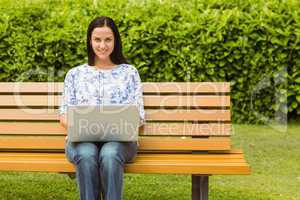 Cheerful brunette sitting on bench using laptop