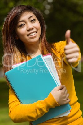 Female college student with books gesturing thumbs up in park