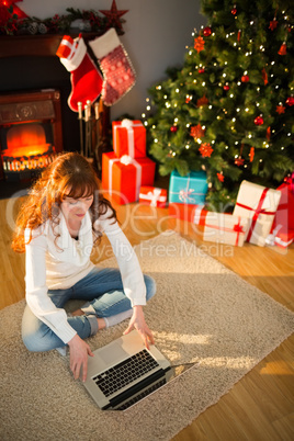 Redhead woman sitting on floor using laptop at christmas