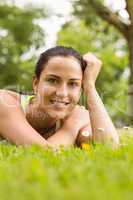 Smiling fit brunette lying on grass and looking at camera