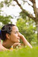 Fit brunette lying and thinking on grass