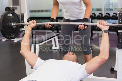 Trainer helping man with lifting barbell in gym