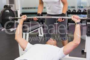 Trainer helping man with lifting barbell in gym