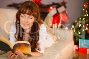 Pretty woman lying on a cosy couch reading book