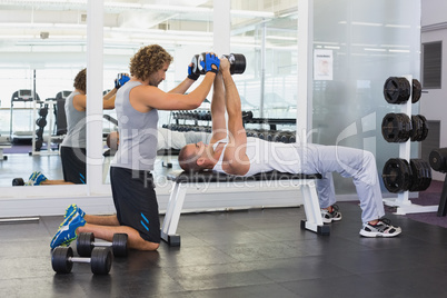 Male trainer assisting young man with dumbbells in gym