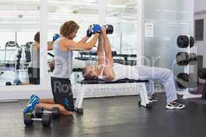 Male trainer assisting young man with dumbbells in gym