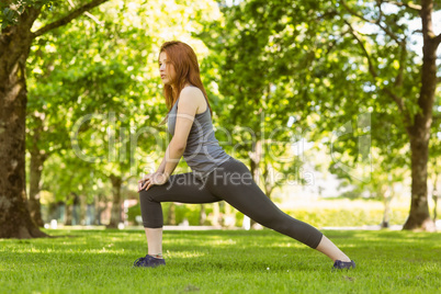 Pretty athletic redhead stretching in park