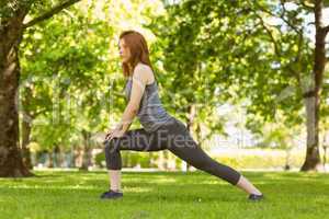 Pretty athletic redhead stretching in park