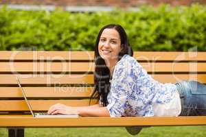 Casual brunette lying on bench typing on laptop