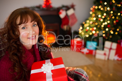 Smiling redhead holding gift on the armchair at christmas