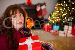 Smiling redhead holding gift on the armchair at christmas