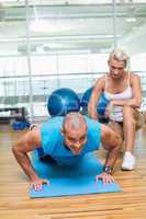 Female trainer assisting man with push ups at gym