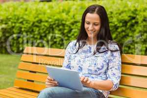 Happy brunette sitting on bench using tablet