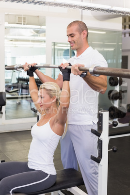 Trainer helping woman with lifting barbell in gym