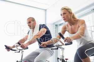 Determined couple working on exercise bikes at gym