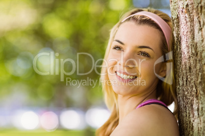 Fit blonde leaning against tree smiling