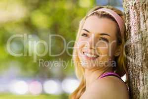 Fit blonde leaning against tree smiling