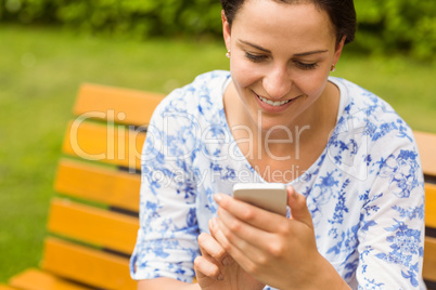 Smiling brunette sitting on bench texting