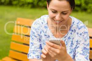 Smiling brunette sitting on bench texting