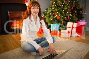 Redhead woman sitting on floor using laptop at christmas