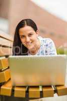 Casual brunette lying on bench using laptop