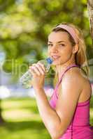 Fit blonde leaning against tree drinking water