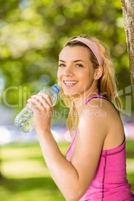 Fit blonde leaning against tree drinking water