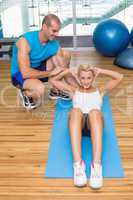 Trainer assisting woman with abdominal crunches at fitness studi