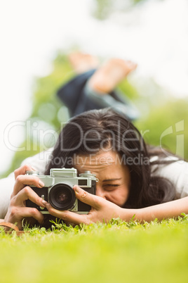 Brunette lying on grass with retro camera taking picture