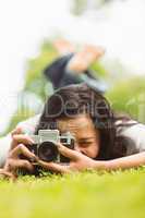 Brunette lying on grass with retro camera taking picture