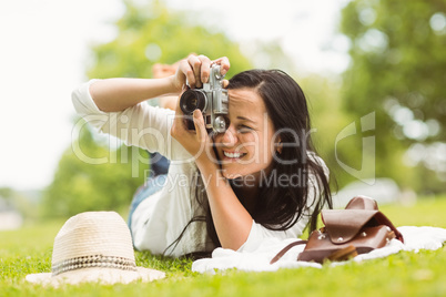 Happy brunette lying on grass taking picture
