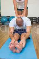 Trainer assisting man with stretching exercises at fitness studi