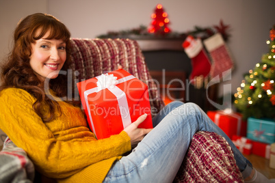 Smiling redhead holding gift on the couch at christmas