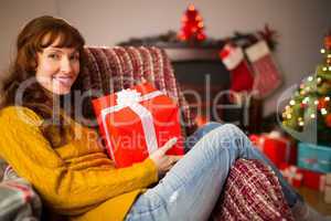 Smiling redhead holding gift on the couch at christmas