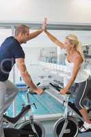 Couple giving high five while working on exercise bikes at gym