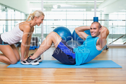 Trainer assisting young man with abdominal crunches at fitness s